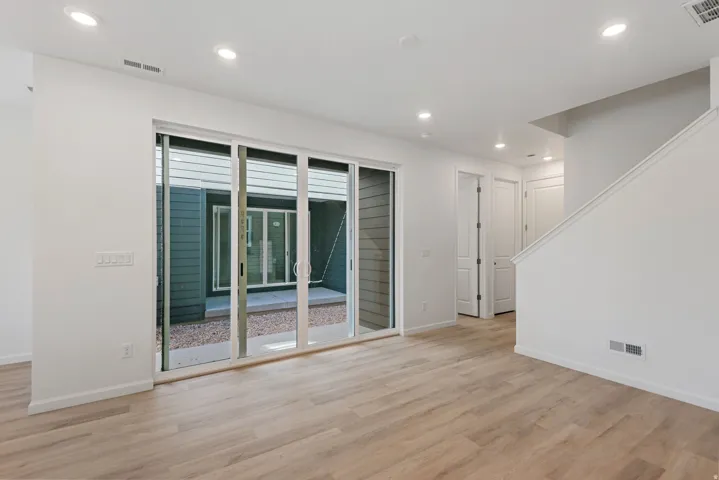 Spacious room featuring wood-finish flooring, recessed lighting, and a sliding glass door opening to an outdoor area with gravel and siding
