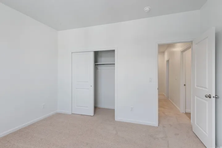 Neutral tone walls and carpeting throughout, featuring a built-in closet with sliding panel doors and interior shelving