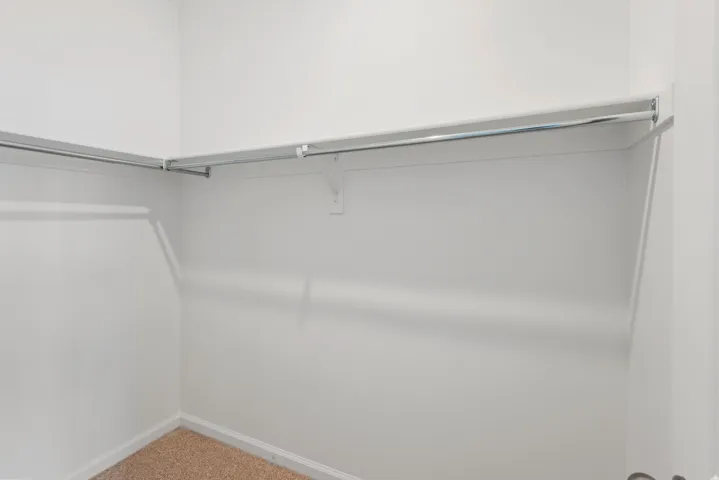 Corner closet with wall-mounted clothing rods and neutral carpeting