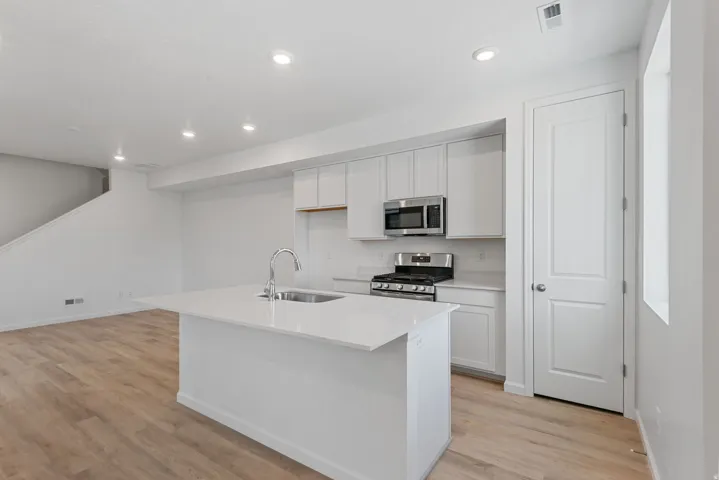 Kitchen featuring a center island with integrated sink, white cabinetry, stainless steel appliances, and light wood-finish flooring