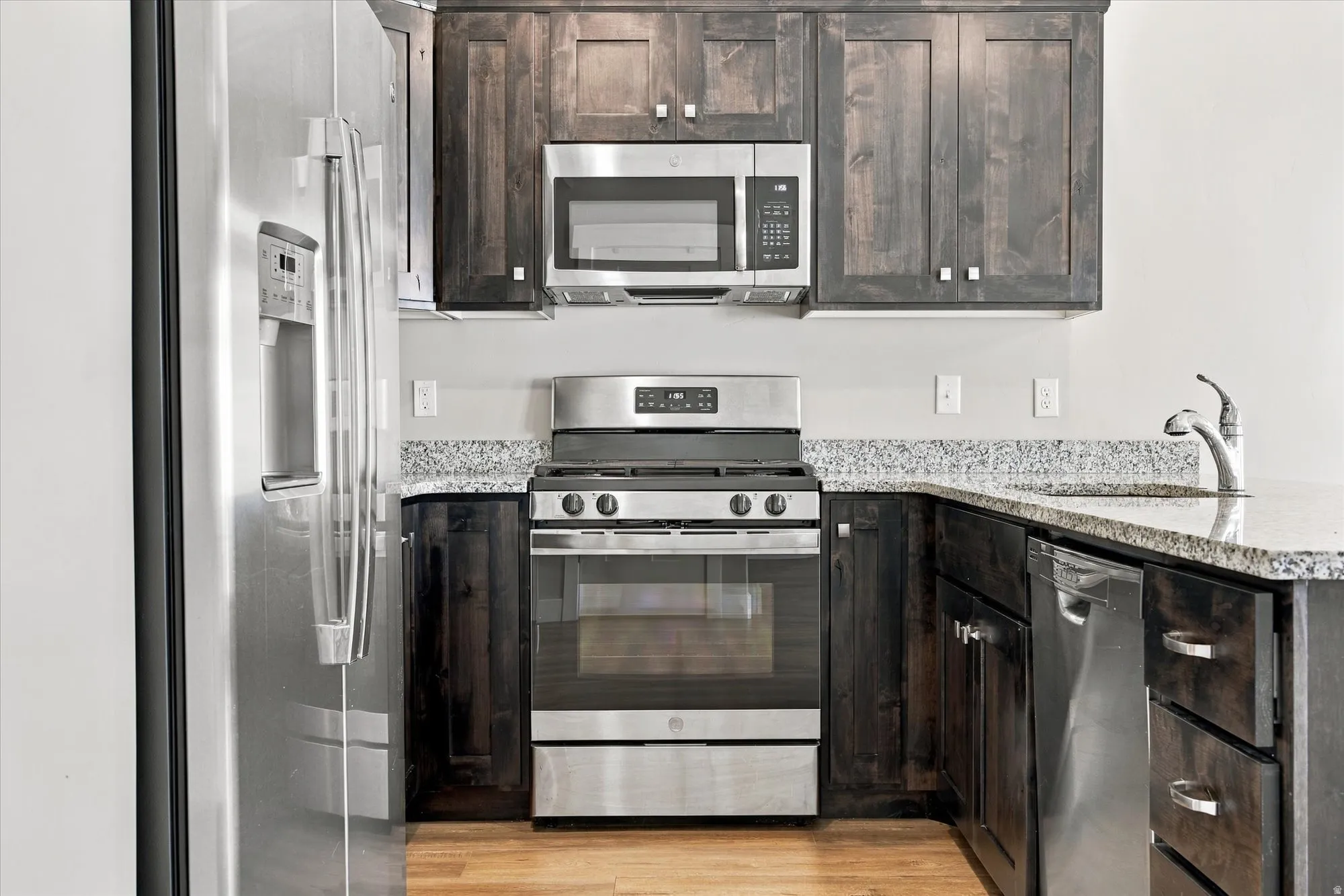 Kitchen featuring dark wood cabinetry, stainless steel appliances, granite countertops, and wood-finish flooring