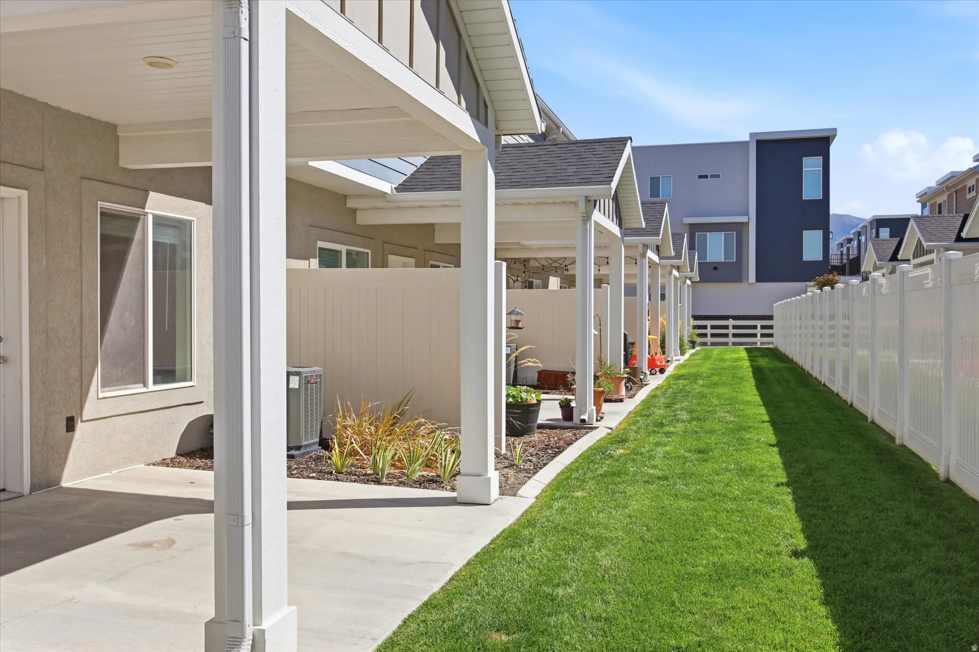 Expansive grassy side yard with white privacy fencing and concrete patios