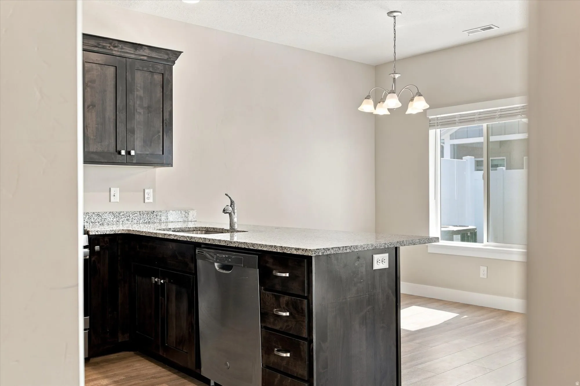 Kitchen featuring dark wood-finish cabinetry, granite countertops, stainless steel sink, and stainless steel dishwasher