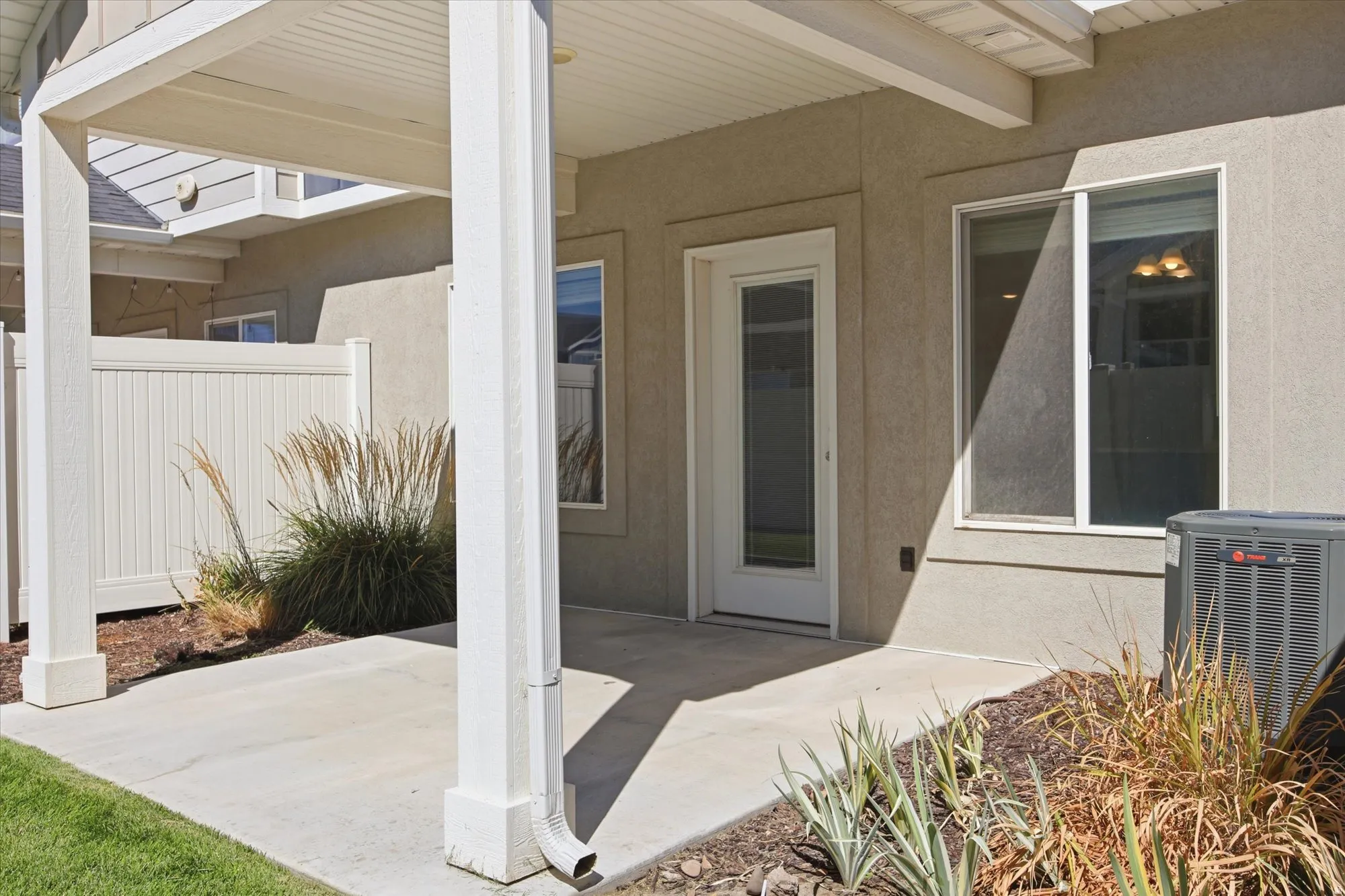 Covered patio with concrete flooring, stucco exterior, and a white vinyl privacy fence