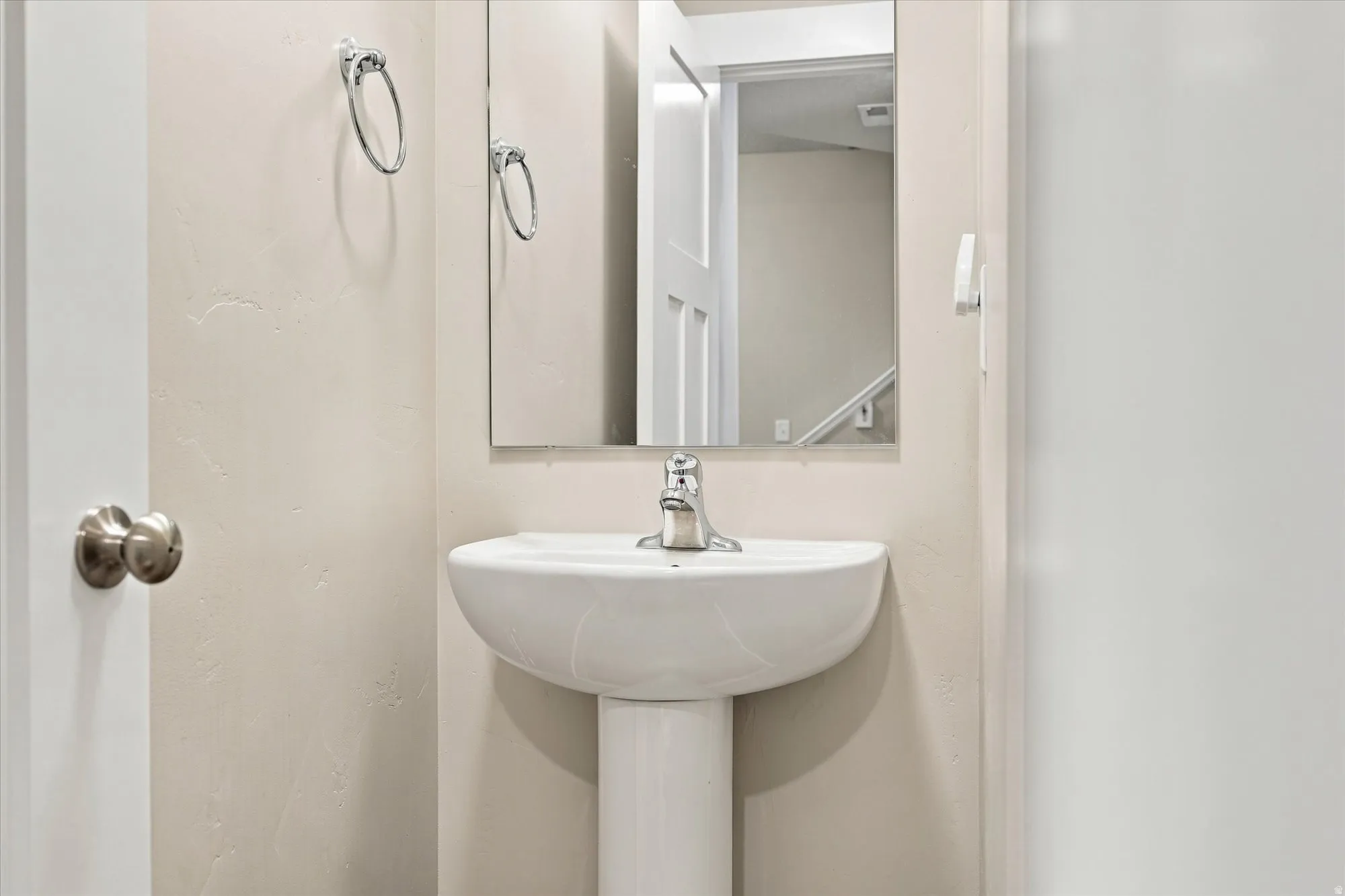 Pedestal sink with a chrome faucet, wall-mounted mirror, and neutral wall finish