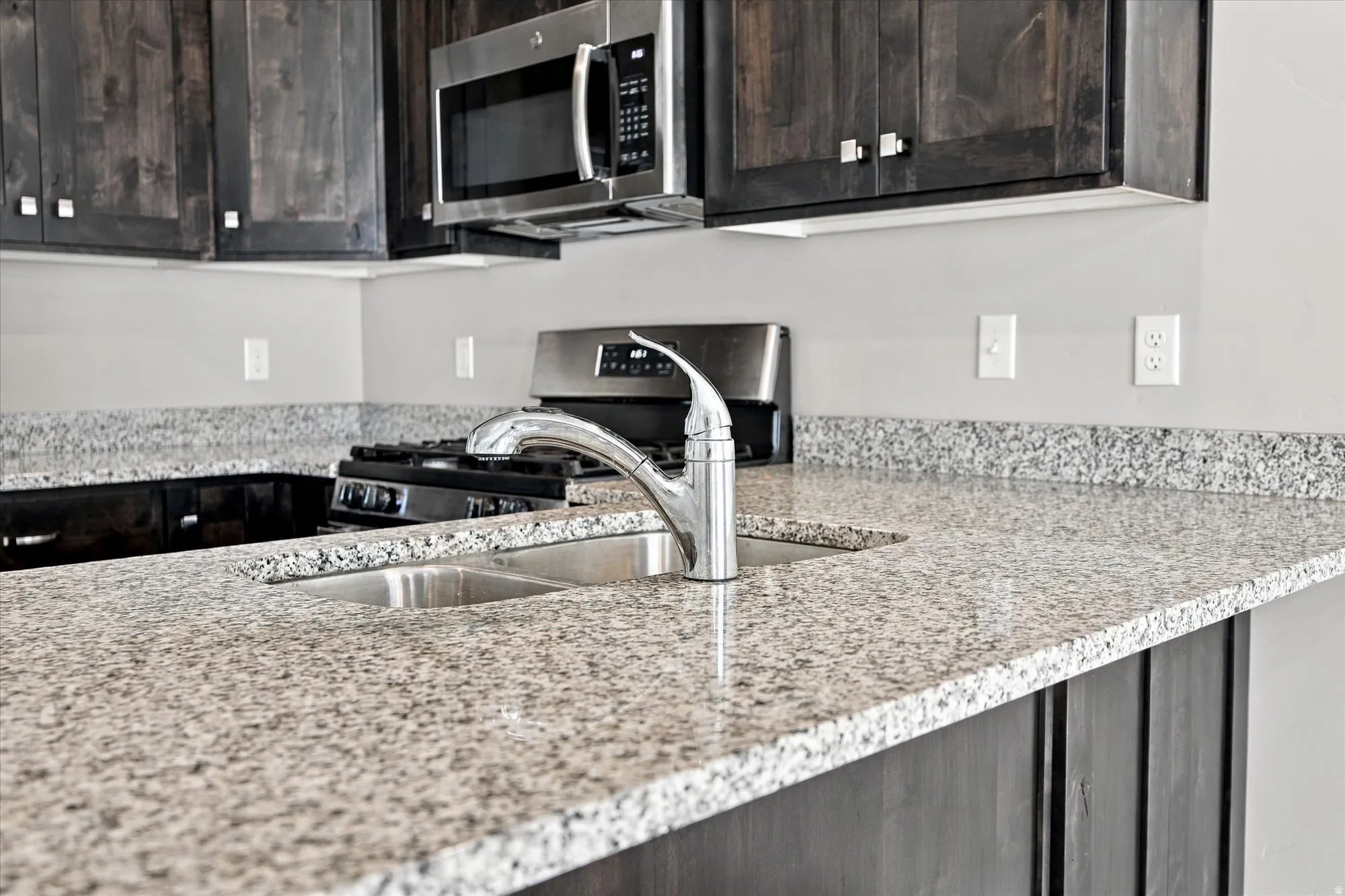 Granite countertops, stainless steel appliances, undermount sink, chrome faucet, and dark wood cabinetry
