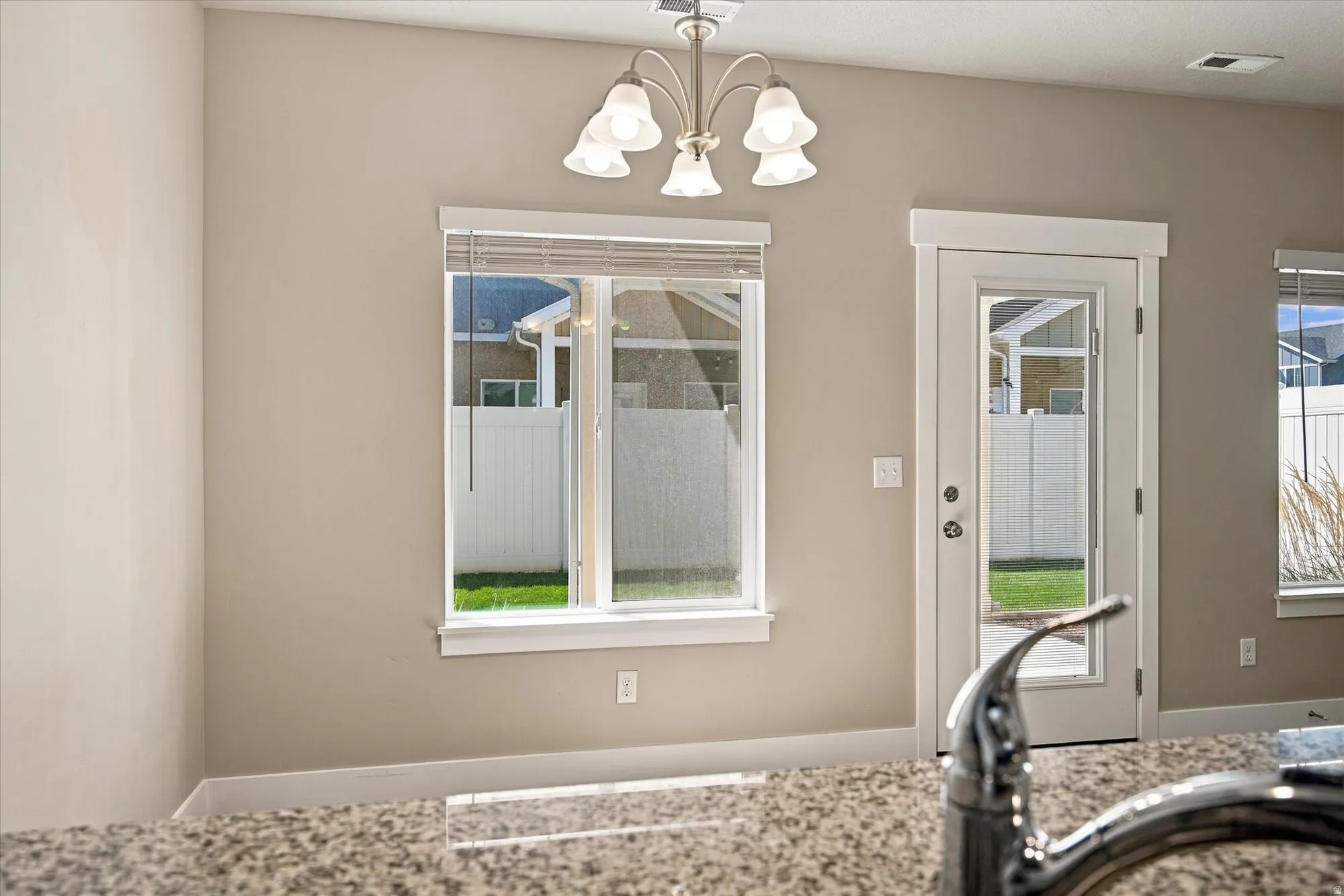 Recessed lighting, central window with blinds, glass-paneled door, and a polished faucet with a speckled countertop