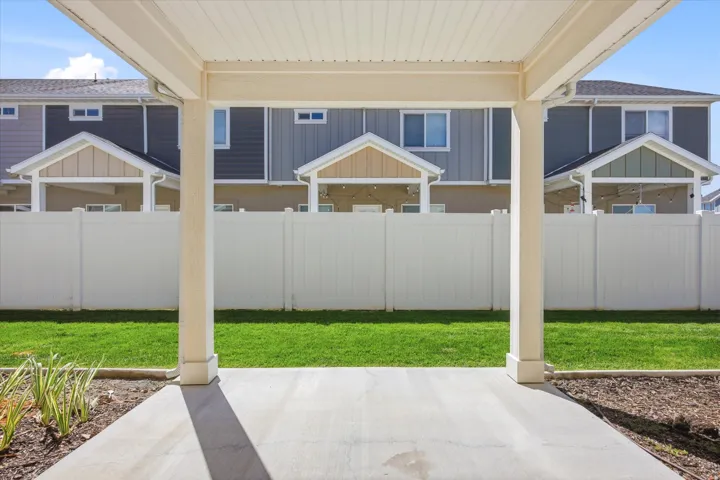 Covered patio with a concrete surface, leading to a fenced backyard with a manicured lawn