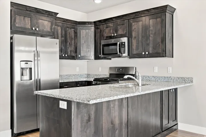 Kitchen featuring dark wood-finish cabinetry, light speckled countertops, stainless steel appliances, and a built-in microwave