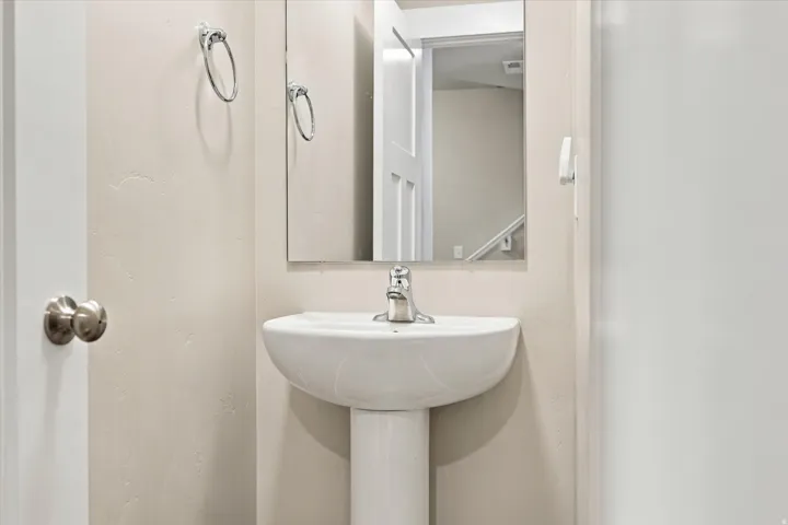 Pedestal sink with a chrome faucet, wall-mounted mirror, and neutral wall finish