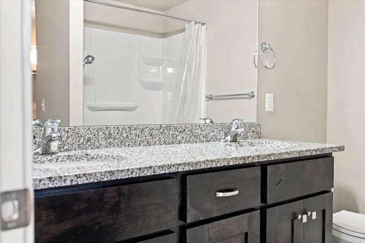 Dual vanity with integrated sinks, speckled countertop, and dark wood-finish cabinetry