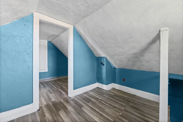Angled ceiling, wood-finish flooring, white trim, and a built-in wall panel