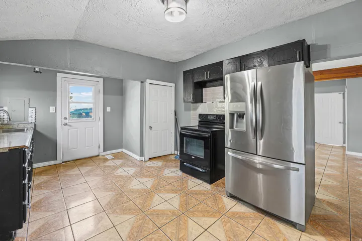 Kitchen featuring stainless steel refrigerator, black electric range, black cabinetry, and tile flooring
