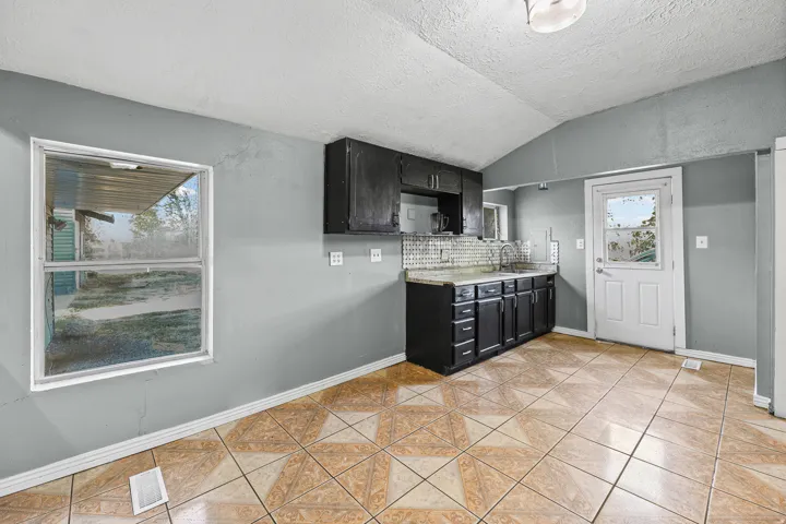 Kitchen featuring dark cabinetry, light-toned tiled flooring, a stainless steel sink, a window, and a white door