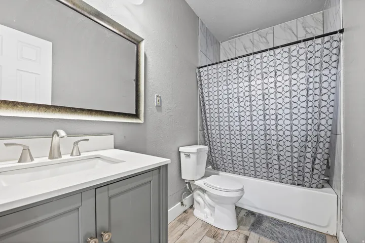 Vanity with integrated sink, brushed nickel faucet, large framed mirror, tiled bath surround, and wood-finish flooring