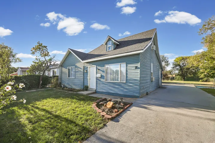 Blue siding exterior with dormer window, established front lawn, concrete driveway, and mature landscaping