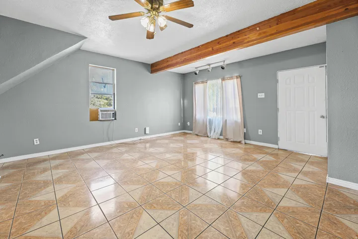 Spacious room featuring patterned tile flooring, a sloped ceiling, and an exposed wood beam