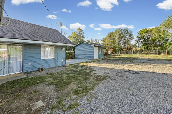 Gravel parking area, separate storage shed, residential structure with horizontal siding, and a shingle roof
