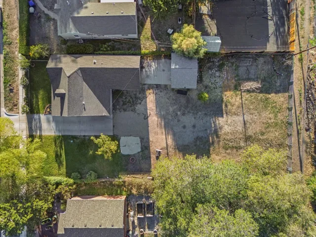 Property featuring a pitched shingle roof, a concrete driveway, and established greenery