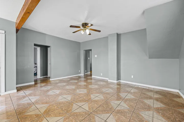 Exposed wood beam, ceiling fan with light fixture, patterned tile flooring, and gray wall finishes