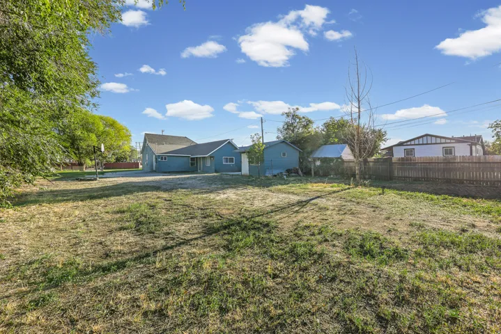 Expansive lot with a multi-structure property, featuring a primary residence with blue siding, a detached shed, and a privacy fence
