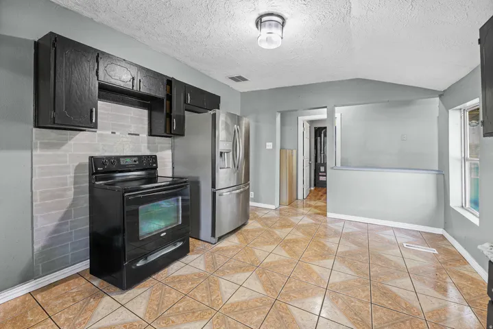 Kitchen featuring patterned tile flooring, black cabinetry, white subway tile backsplash, and stainless steel refrigerator