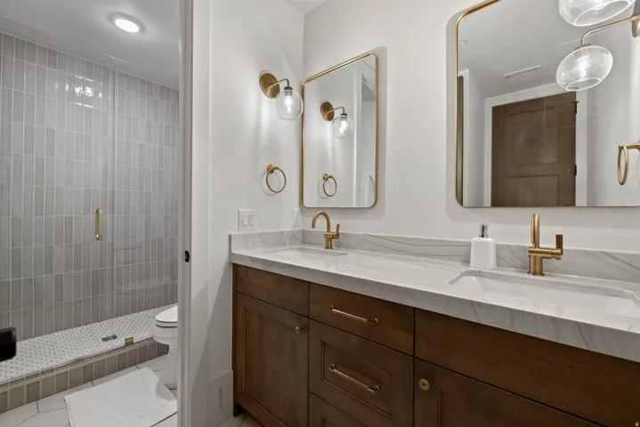 Dual vanity with integrated sinks, wood-finish cabinetry, and gold-finish fixtures