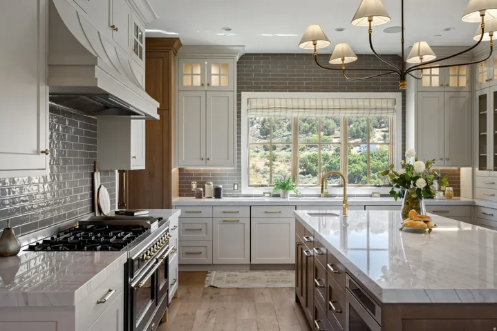 Spacious kitchen featuring a large central island, light-toned cabinetry, light wood-finish flooring, a stainless steel range, and a brass-finish faucet