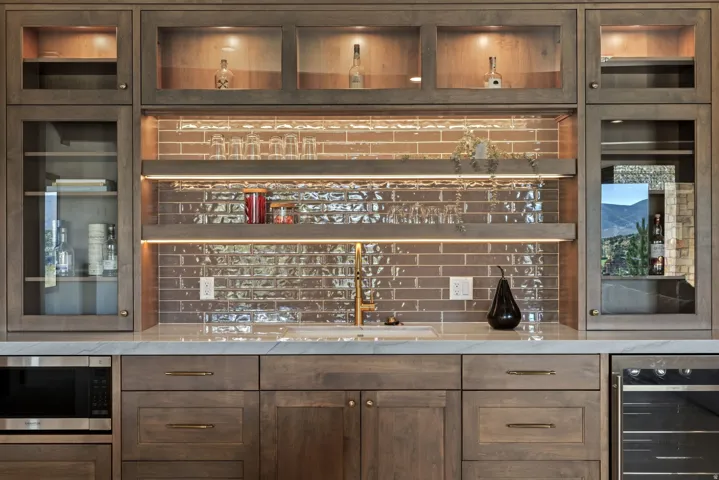 Built-in cabinetry with glass-front uppers, under-cabinet lighting, and a subway tile backsplash
