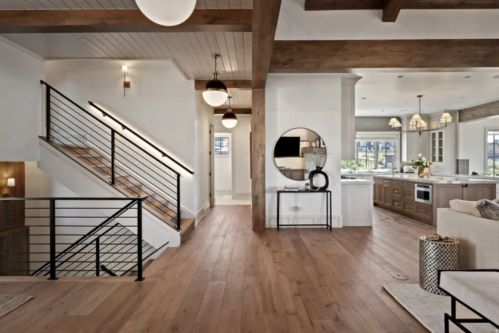 Hardwood flooring throughout, exposed wood ceiling beams, modern black metal stair railing, built-in kitchen island microwave, and pendant lighting fixtures
