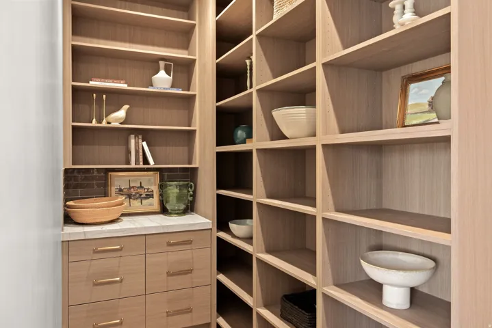 Extensive custom built-in shelving with light wood-finish cabinetry, a white countertop, and integrated drawers with gold-tone hardware