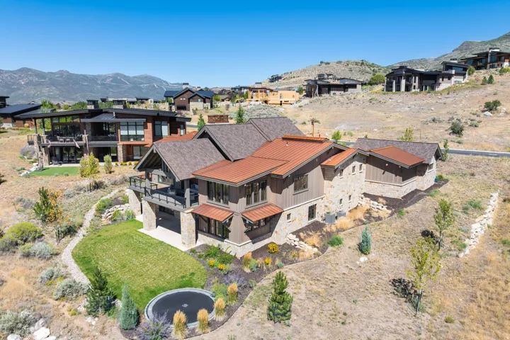 Multi-level residence featuring stone and wood-panel siding, a combination shingle and metal roof, upper-level balcony, and a manicured lawn area