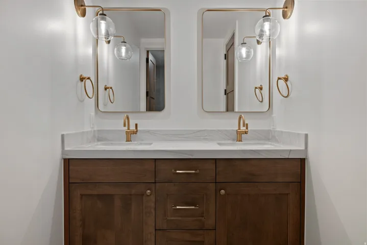 Dual vanity with dark wood-finish cabinetry, white countertop, and gold-toned fixtures