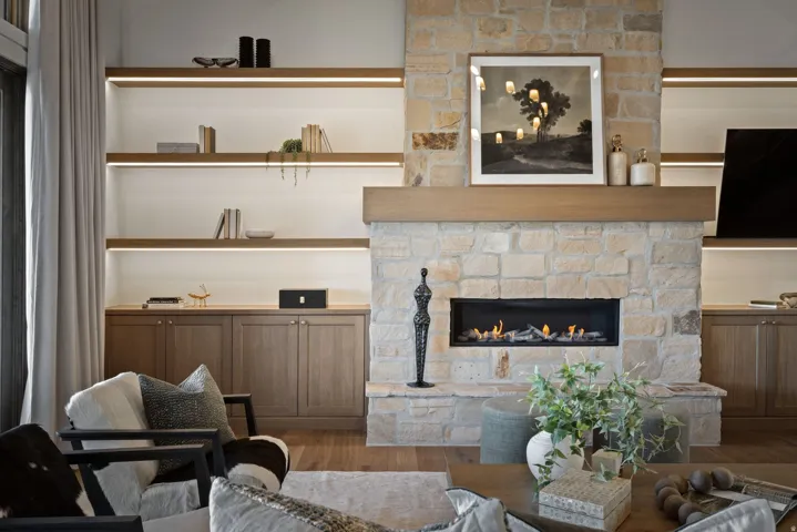 Stone-clad fireplace with a recessed linear gas insert, flanked by built-in cabinetry and illuminated shelving