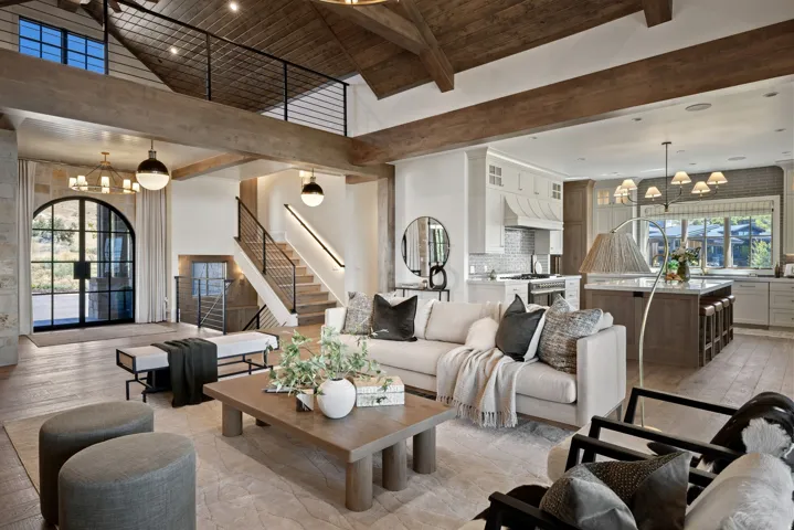 Open-concept living space featuring wood-finish flooring, exposed ceiling beams, a gourmet kitchen with a large island, and a distinctive arched glass door