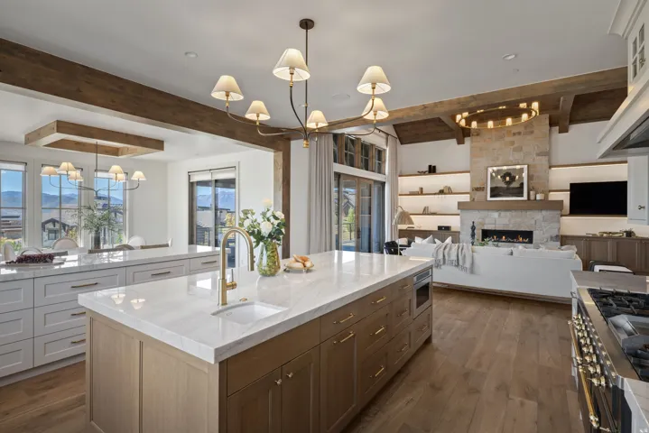 Spacious kitchen island with an undermount sink and gold-tone faucet, wood-finish flooring, exposed ceiling beams, and a stone-clad fireplace