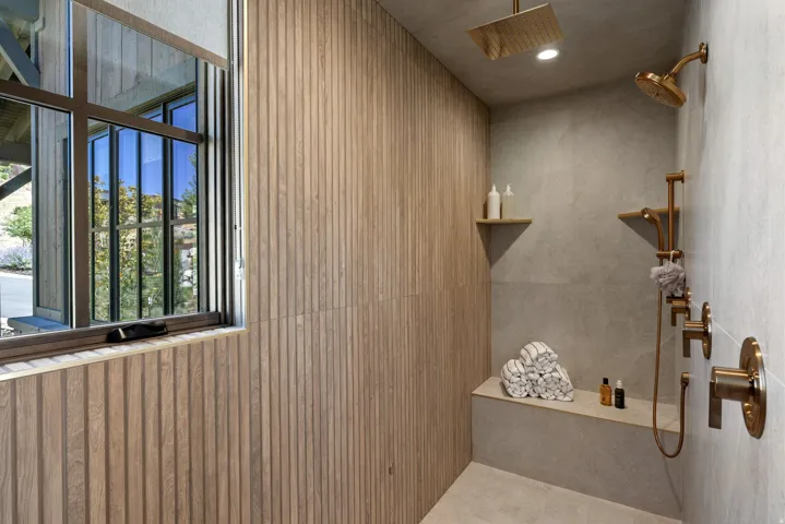 Shower with wood-finish paneling, an integrated bench, a rain shower head, and an additional shower head with matching bronze-tone fixtures