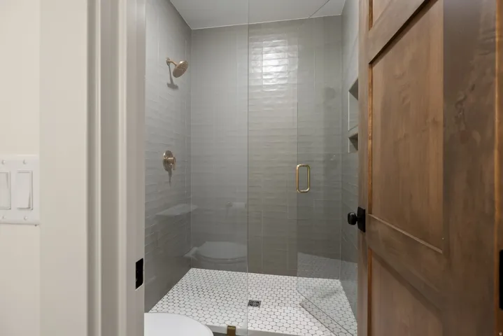 Glass-enclosed shower featuring a gold-finish shower head and controls, textured subway tile, and hexagonal floor tiles