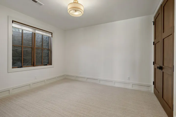 Carpeted flooring, white walls, wainscoting, wood-finish window trim, and a wood-finish door