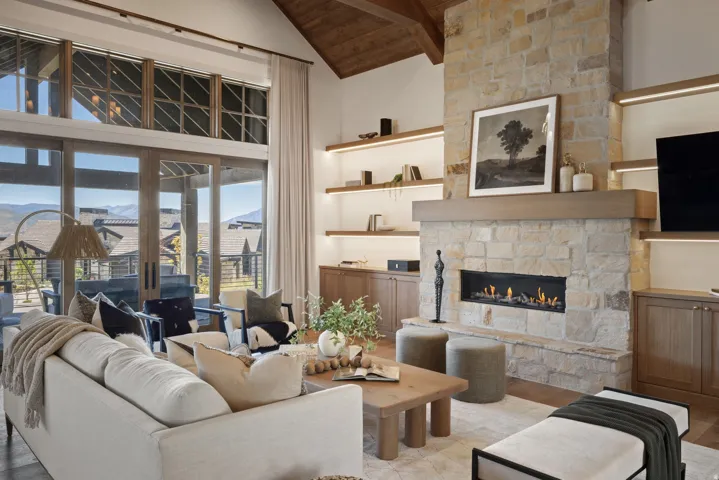 Vaulted wood-clad ceiling, stone-clad fireplace with gas insert, built-in shelving with integrated lighting, wood-frame sliding glass doors, and transom windows