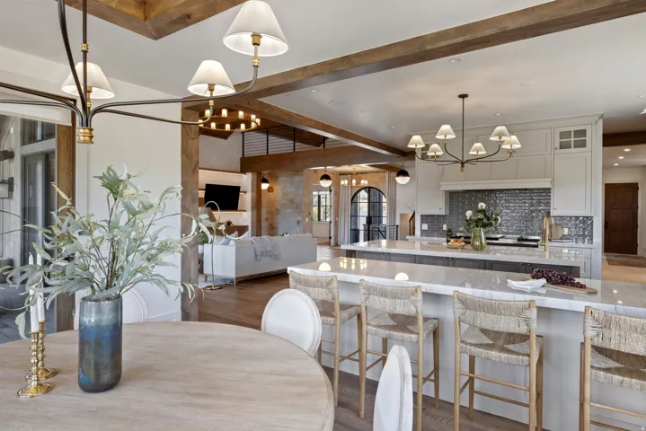Open-concept living space with exposed wood beams, a spacious kitchen island, custom cabinetry, and a textured tile backsplash