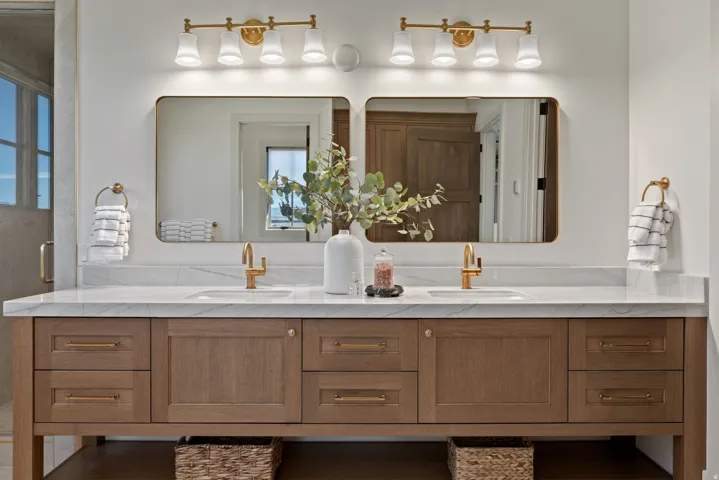 Dual-sink vanity featuring a light wood finish, white countertop, gold-toned hardware, and rectangular mirrors