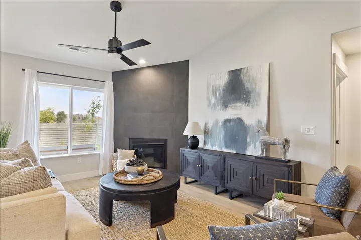 Integrated fireplace with a dark tile surround, large window with natural light, wood-finish flooring, and a modern ceiling fan