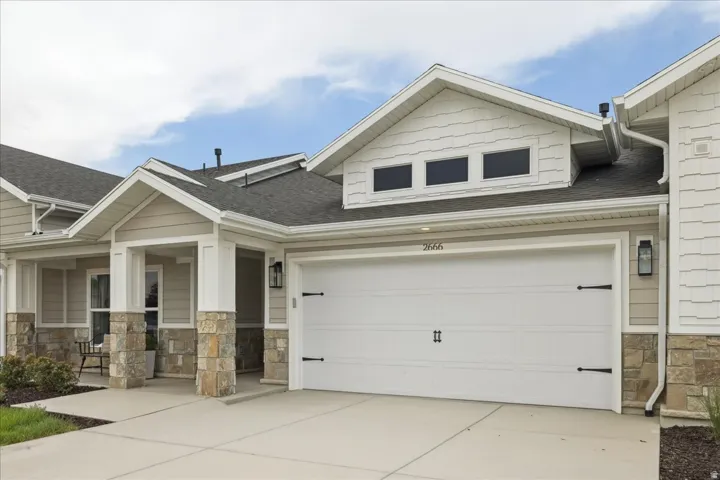 Exterior featuring a white garage door with decorative hardware, an asphalt shingle roof, stone accents, light-toned siding, and a concrete driveway