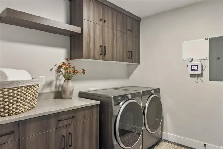 Laundry area featuring wood-finish cabinetry, a floating shelf, light-toned countertop, and integrated appliances