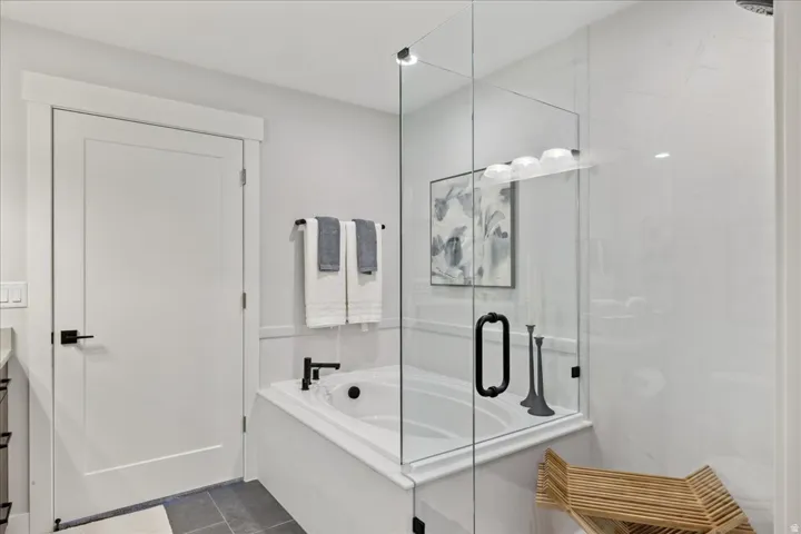 Enclosed soaking tub with matte black fixtures, glass shower surround, and tile flooring