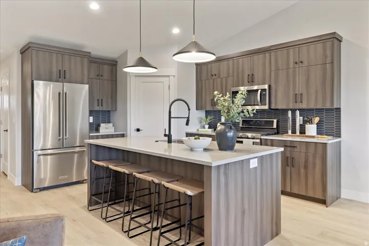 Kitchen featuring wood-finish cabinetry, stainless steel appliances, a center island with countertop seating, a dark tile backsplash, and recessed lighting