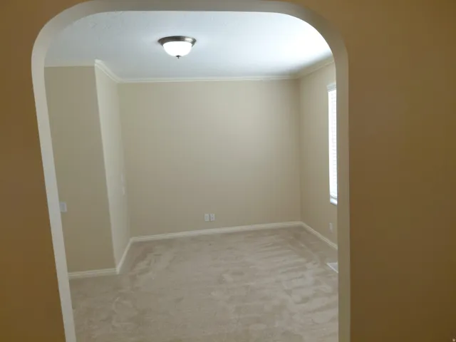 Arched entryway leading to a room with neutral-toned walls, crown molding, and carpeted flooring