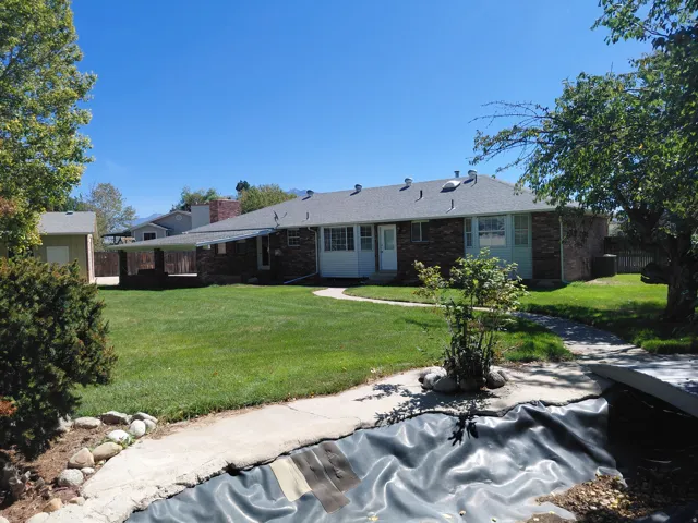 Manicured lawn, mature trees, brick exterior, covered patio, and a detached shed