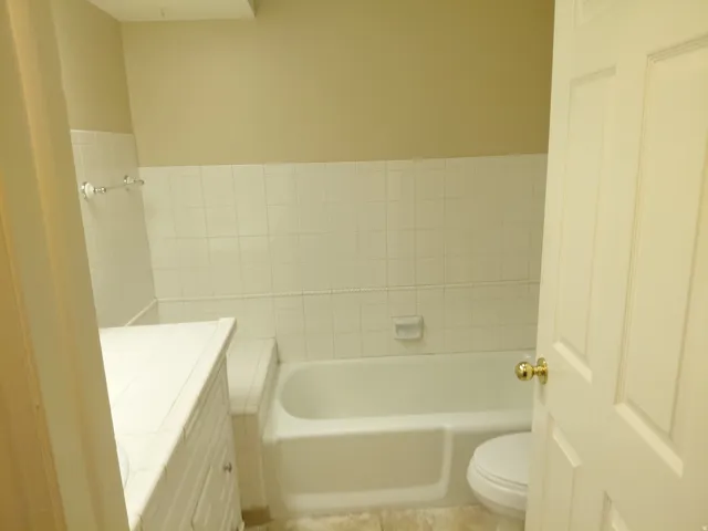 White tiled walls, built-in bathtub, and a paneled vanity with a tiled countertop